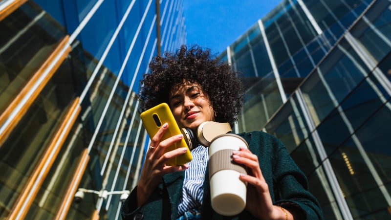 Mobilfunknetz: Eine junge Frau nutzt ihr Smartphone vor einem Bürogebäude mit Glasfassade