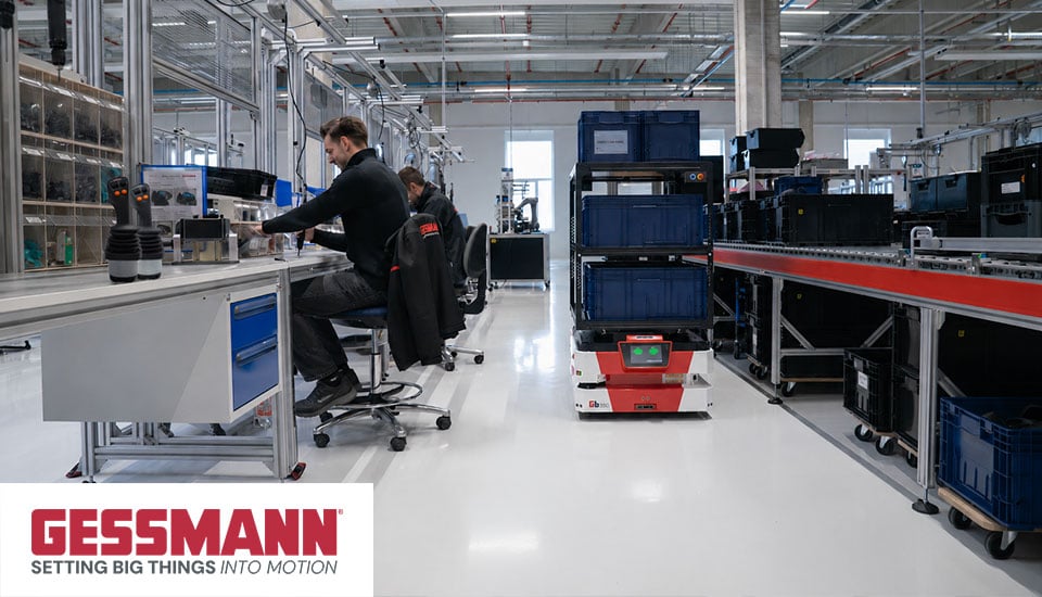 Gessmann Produktionsumgebung mit Mitarbeitern, Joystick-Bedienpult und autonomem mobilen Roboter (AMR), Logo „GESSMANN – setting big things into motion"