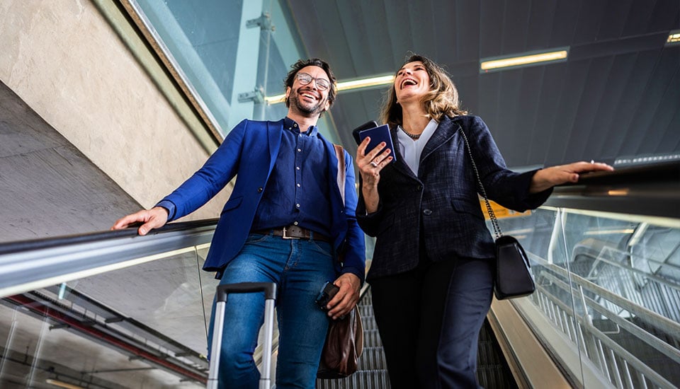 Zwei Geschäftsreisende auf einer Rolltreppe in einem Gebäude nutzen ihr Smartphone mit stabilem Mobilfunkempfang