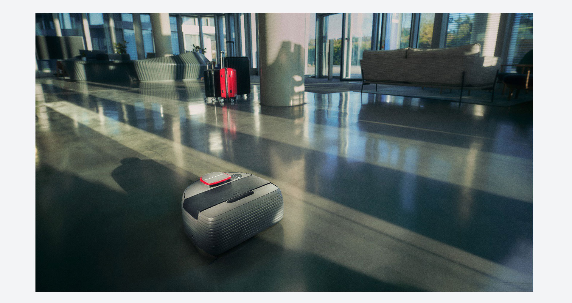 nexaro-content4.jpg Autonomer Reinigungsroboter von Nexaro fährt durch eine helle Hotellobby mit glänzendem Boden und Koffern im Hintergrund.