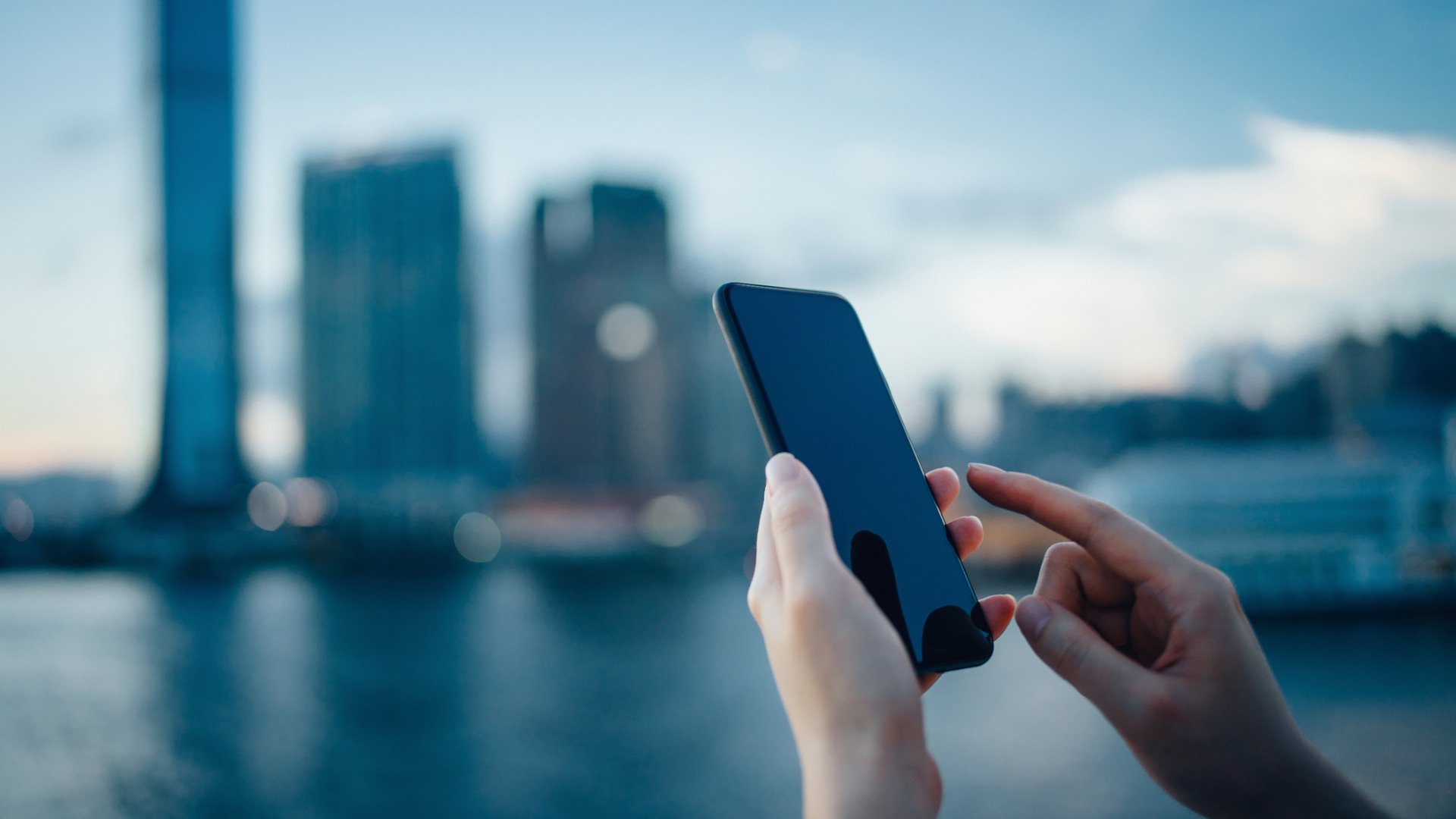 Nahaufnahme eines Smartphones in den Händen einer Frau vor der Silhouette einer großen Stadt