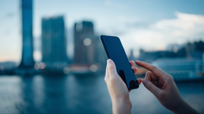 Nahaufnahme eines Smartphones in den Händen einer Frau vor der Silhouette einer großen Stadt