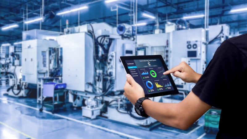 Ein Mitarbeiter steuert in einer Fertigungsanlage vernetze Maschinen per Tablet