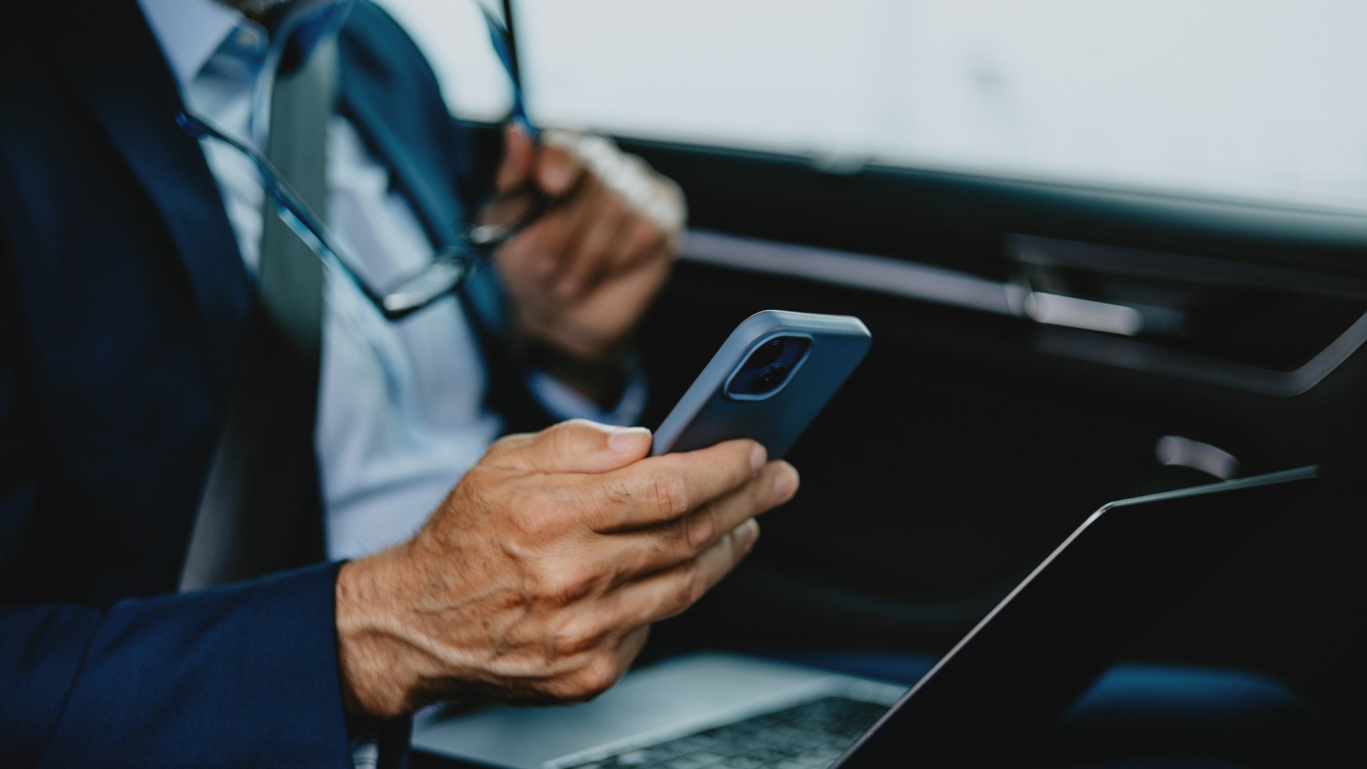 Geschäftsmann mit iPhone und Laptop in einem Auto