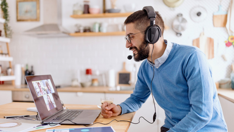 Ein Mann mit Headset nimmt mit einem Laptop an einem Videocall teil.