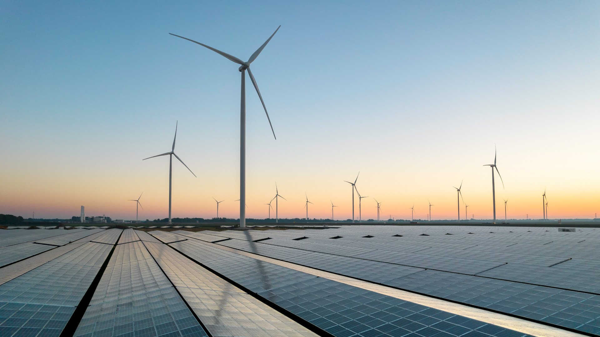 Wind- und Solarkraftanlagen im Sonnenaufgang vor der Skyline einer Stadt