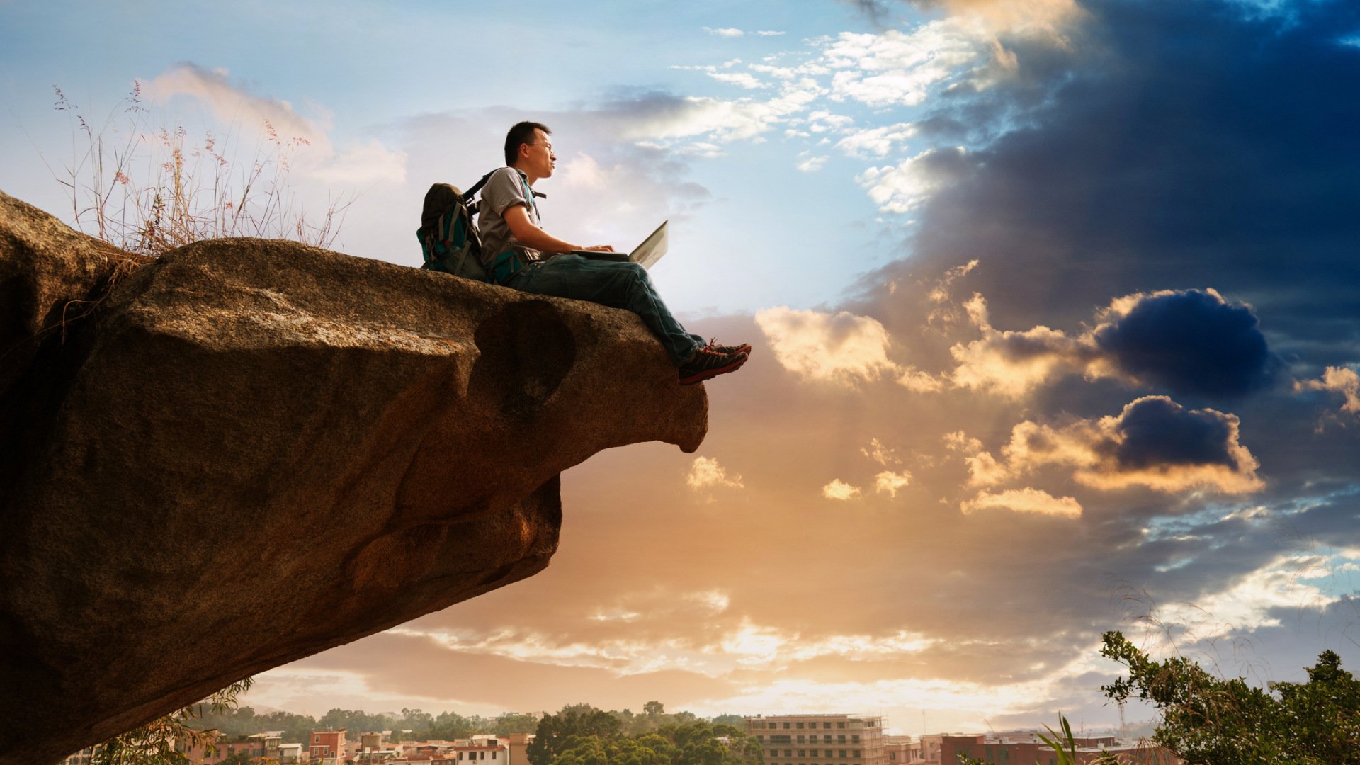 Ein Mann mit Laptop sitzt am Rand einer Klippe