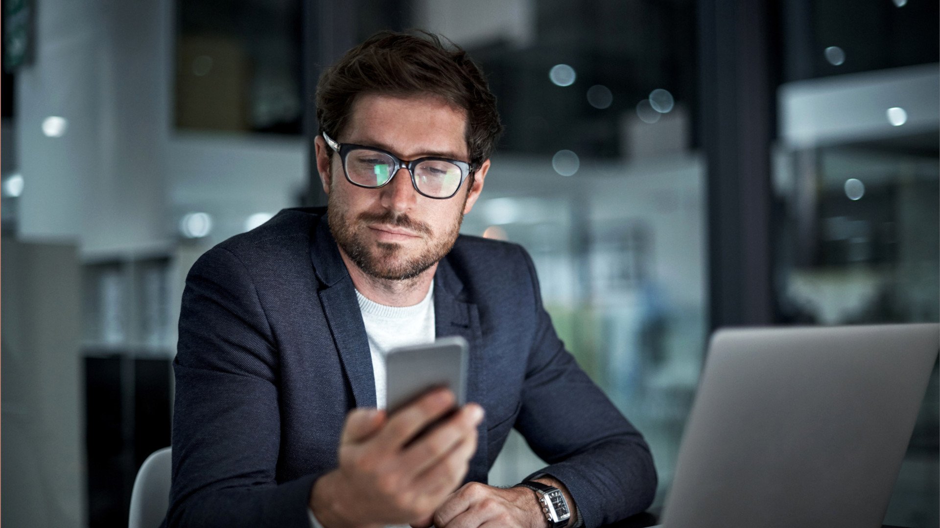 Mann im Büro arbeitet mit Smartphone und Notebook