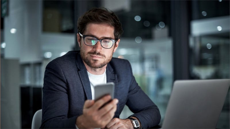 Mann im Büro arbeitet mit Smartphone und Notebook