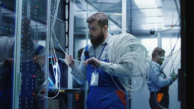 Ein Mann arbeitet in einem Serverraum an einem Glasfaseranschluss