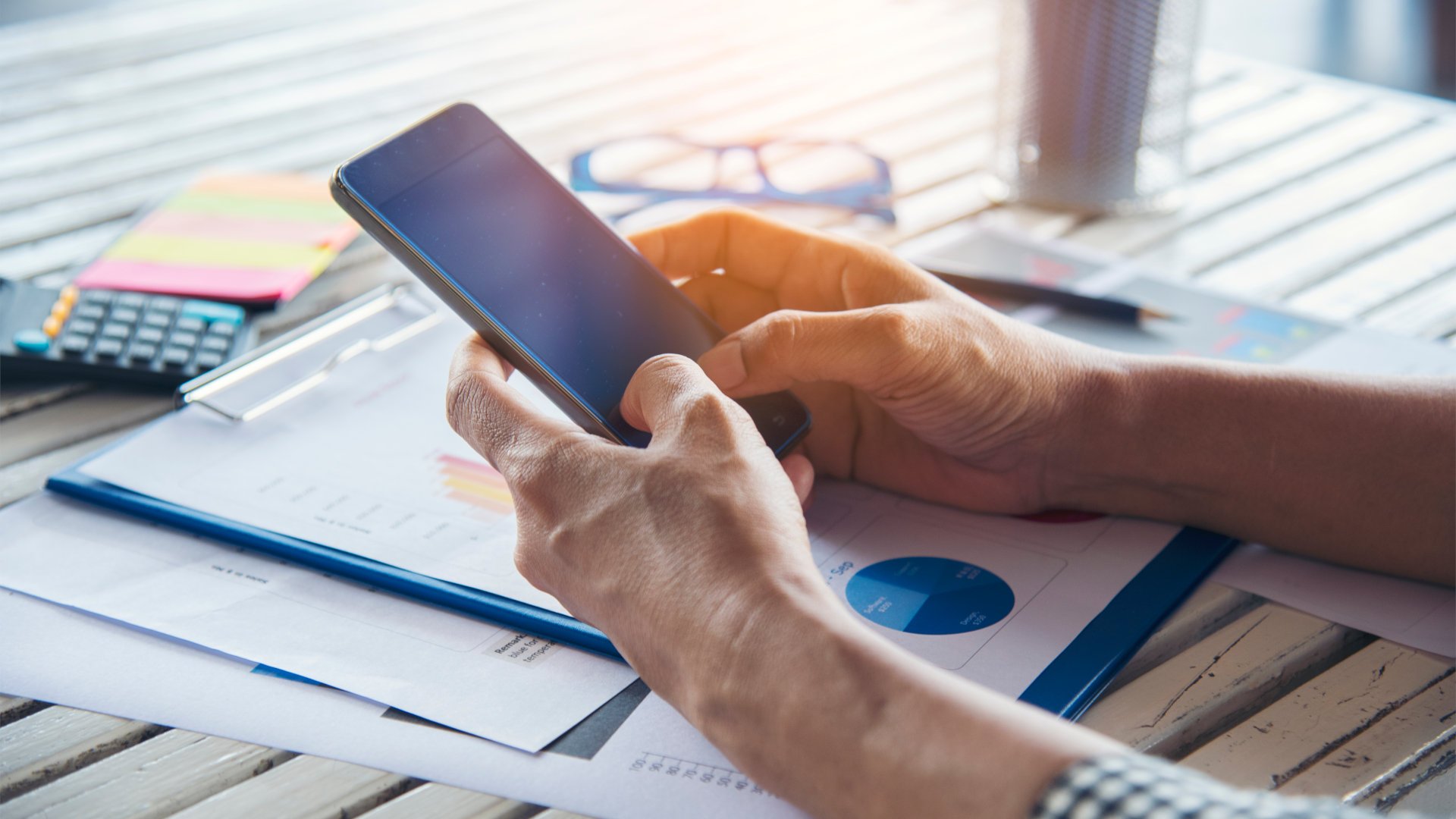Eine Frau hält ein Smartphone in den Händen während sie über Unterlagen sitzt