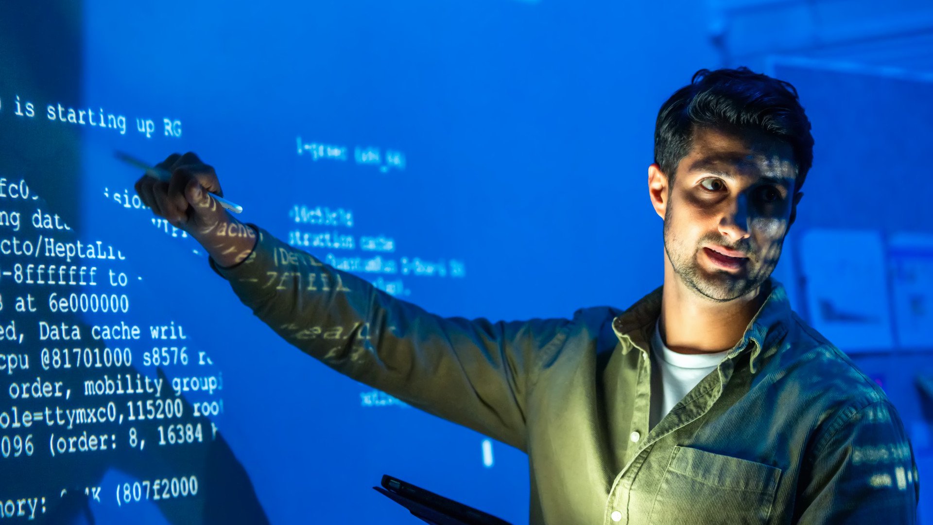 Ein IT-Experte deutet auf Code, der an eine Wand projiziert wird.