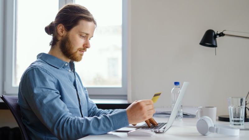 Ein Mitarbeiter gibt  im Büro Kreditkartendaten in seinen Laptop ein.