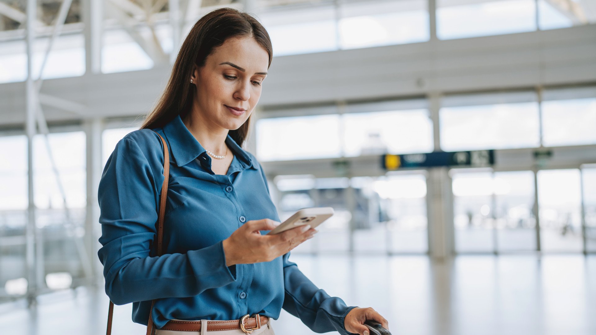 Eine Geschäftsfrau schaut am Flughafen auf ihr Smartphone.