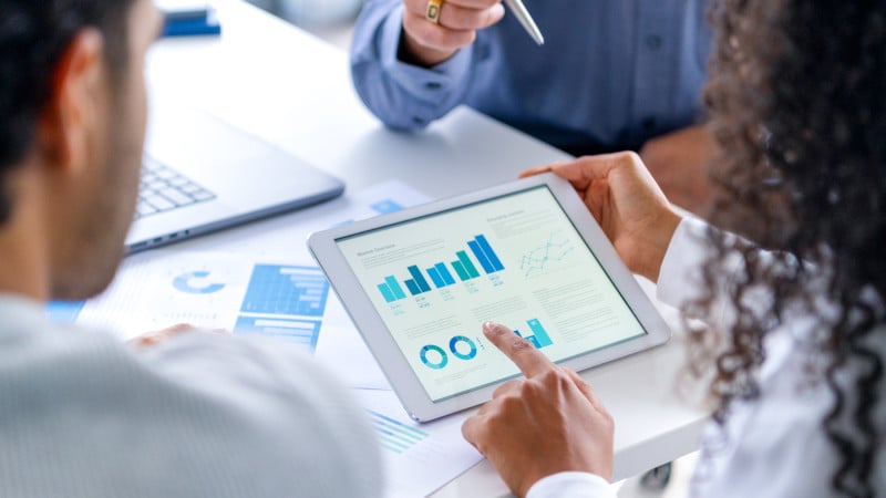 Nahaufnahme: Drei Menschen schauen Daten-Diagramme auf einem Tablet an