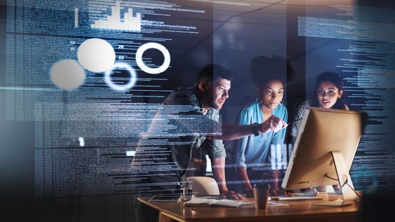 Mitarbeitende blicken auf einen Computer, Overlay mit Software-Code