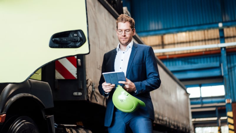 Telematik: Ein Mann im Anzug nutzt ein Tablet, während er neben einem LKW steht