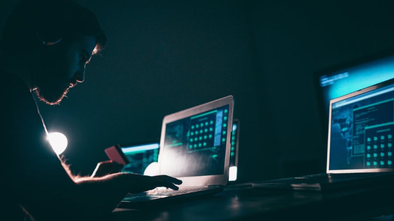 Ein Mann sitzt im Dunkeln vor mehreren Laptops