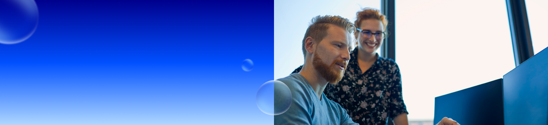 Abbildung: Ein Mann sitzt an einem PC und eine Frau schaut ihm stehend zu