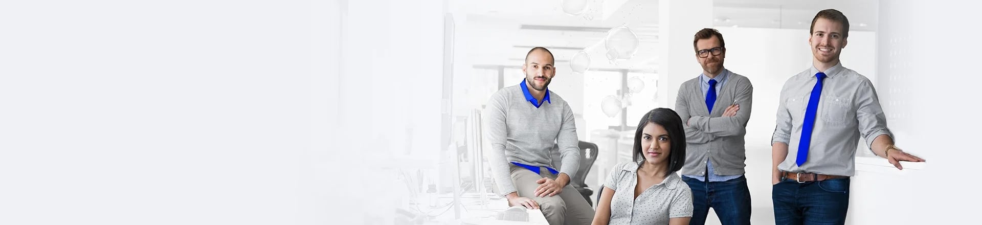 Vier Personen stehen und sitzen gemeinsam in einem Büro und posieren vor einem hellen Hintergrund.